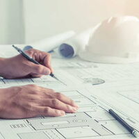 Zwei Hände von links notieren etwas auf einem Bauplan. Im Hintergrund liegt ein Helm.