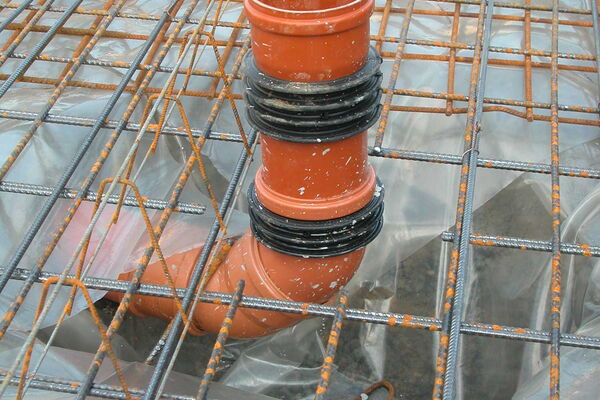 Ein gebogenes Kunststoffrohr kommt aus dem Boden zwischen Stahlgitter hervor.