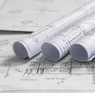 Nahaufnahme von Bauplänen auf welchen Wiederrum zusammengerollte Baupläne liegen.