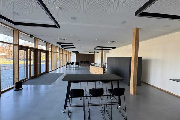 Innenansicht eines großen Raumes mit großer Fensterfront links. Versetzt sind Stühle. mit Tischen zu sehen.