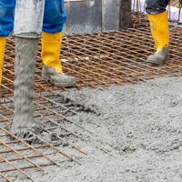 2 Personen angeschnitten knieabwärts zu sehen in gelben Gummistiefeln auf Stahlgerüst mit flüssigem Beton.