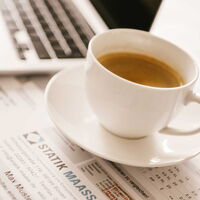 Kaffeetasse steht auf Zeichenplänen - im Hintergrund ist ein Laptop zu sehen.