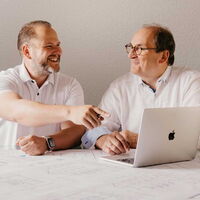 Die Geschäftsführer links Ingo Maaß und rechts Klaus Maaß sitzen vor einem Laptop und besprechen sich.