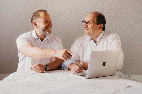 Die Geschäftsführer links Ingo Maaß und rechts Klaus Maaß sitzen vor einem Laptop und besprechen sich.