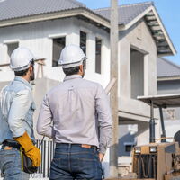 2 Männer mit Helm sind von hinten zu sehen und Blicken auf ein Bauprojekt.
