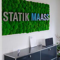 Moosbild mit dem Statik Maass Schriftzug hängt an einer Wand mit moderner Büroeinrichtung.